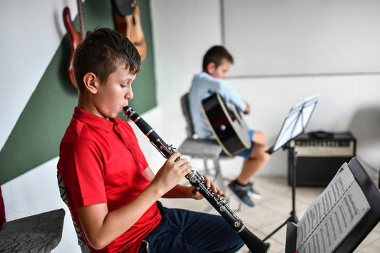 Boy playing clarinet with another child playing guitar in the background