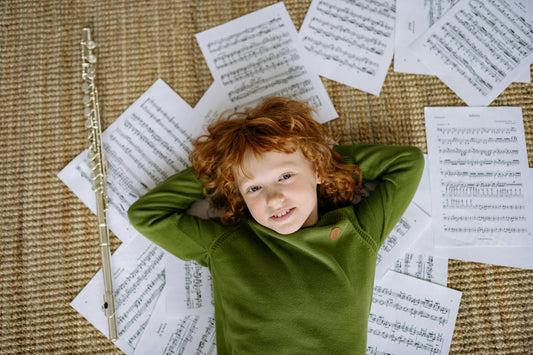 boy laying on floor next to flute and sheet music