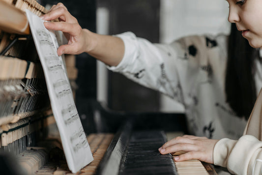 Child at piano with sheet music and teacher