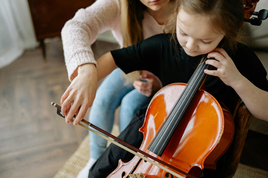 Girl being help by teacher to play cello